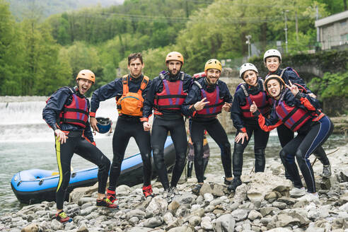 Gruppe verspielter Freunde bei einem Raftingkurs, die am Boot posieren - FBAF00743