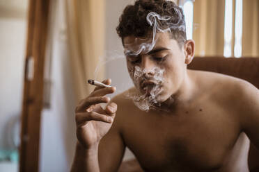 Mann mit nacktem Oberkörper, der einen Joint mit Marihuana raucht - ACPF00548