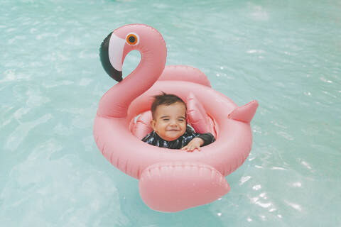 Unbekümmertes Baby in rosa Flamingo schwimmt im Schwimmbad, lizenzfreies Stockfoto