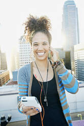 Mixed race woman listening to earbuds on urban rooftop - BLEF07080