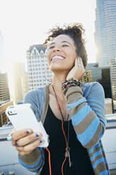 Mixed race woman listening to earbuds on urban rooftop - BLEF07081