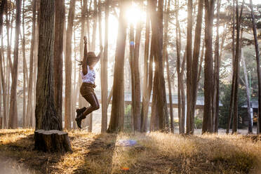 Black woman jumping from stump in sunny forest - BLEF07108