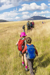 Kaukasische Kinder, die auf einer Wiese in einer abgelegenen Landschaft spazieren gehen - BLEF07163