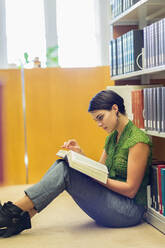 Gemischtrassiger Student liest ein Buch in der Bibliothek - BLEF07175