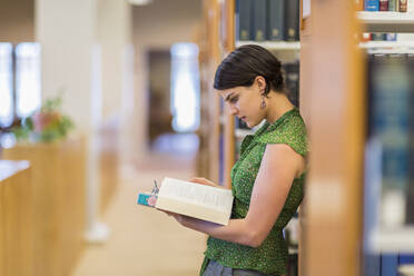 Gemischtrassiger Student liest ein Buch in der Bibliothek - BLEF07178