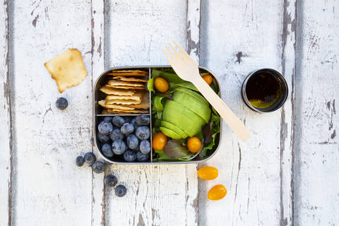 Lunchbox with salad, avocado and yellow tomato, cracker, blueberry and salad dressing, from above stock photo