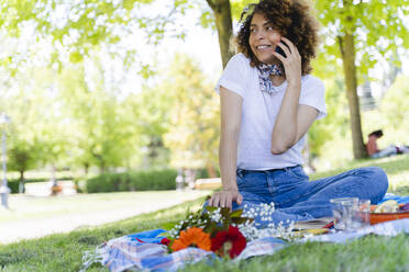 Entspannte Frau mit Mobiltelefon beim Picknick im Park - FMOF00695