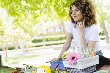 Entspannte Frau mit Mobiltelefon und Kopfhörern beim Picknick im Park - FMOF00704