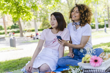 Two women with cell phone and earphones in park - FMOF00712