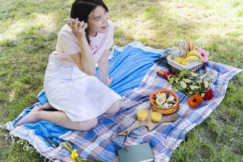 Entspannte Frau, die ein Handy benutzt und ein Picknick im Park macht - FMOF00730