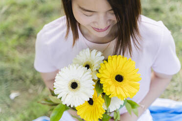 Smiling young woman holding flowers in park - FMOF00733