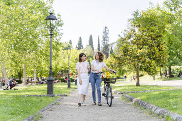 Zwei Frauen mit Fahrrad gehen im Park spazieren - FMOF00736