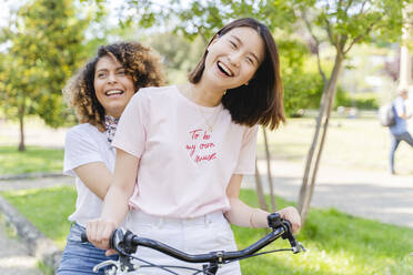 Two happy women on bicycle in park - FMOF00738