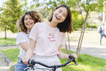 Zwei glückliche Frauen auf dem Fahrrad im Park - FMOF00738