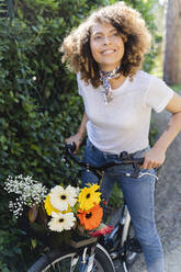Lächelnde Frau mit Blumen und Fahrrad im Park - FMOF00746
