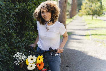 Porträt einer lächelnden Frau mit Blumen und Fahrrad im Park - FMOF00747