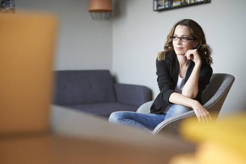 Brünette Frau sitzt auf einem Sessel zu Hause und schaut weg, lizenzfreies Stockfoto