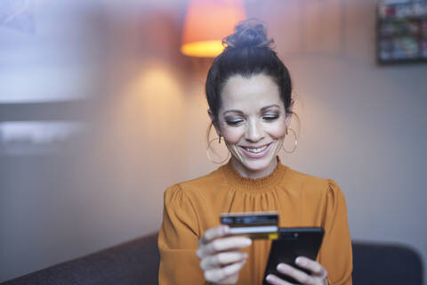 Lächelnde Frau benutzt Smartphone und Kreditkarte zu Hause, lizenzfreies Stockfoto