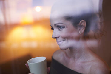 Portrait of brunette woman with cup behind windowpane looking away - PNEF01650