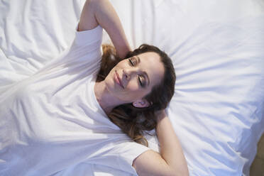 Smiling woman lying in bed with closed eyes - PNEF01656