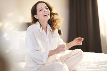 Laughing woman sitting on bed - PNEF01674