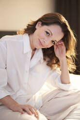 Portrait of smiling woman sitting on bed - PNEF01677