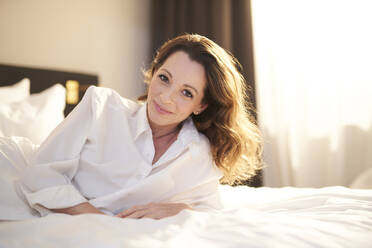 Portrait of smiling woman lying on bed - PNEF01678