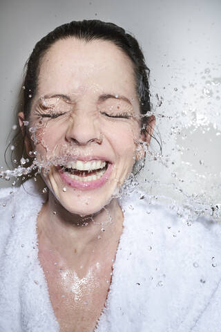 Wasser spritzt in das Gesicht einer glücklichen Frau im Bademantel, lizenzfreies Stockfoto