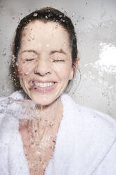 Wasser spritzt in das Gesicht einer glücklichen Frau im Bademantel - PNEF01681