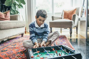 Gemischtrassiger Junge spielt Tischfußball auf dem Wohnzimmerboden - BLEF07196