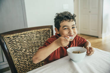 Gemischtrassiger Junge isst Müsli am Tisch - BLEF07222