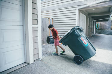 Gemischtrassiger Junge zieht Mülleimer in der Einfahrt - BLEF07223