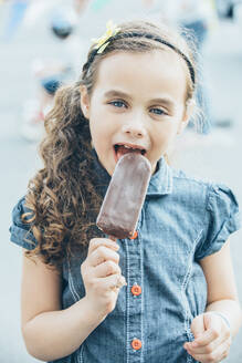 Gemischtrassiges Mädchen isst Eis am Stiel auf der Straße - BLEF07229