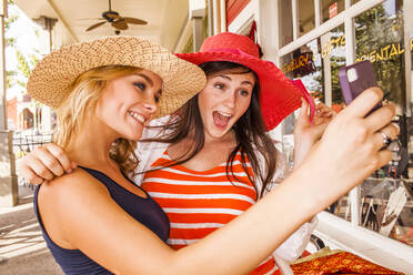 Caucasian teenage girls taking cell phone selfie in hats - BLEF07247