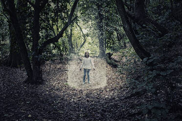 Gemischtrassiges Mädchen steht im Lichtkegel im Wald - BLEF07264