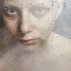 Kaukasische Frau blickt durch nasses Glas - BLEF07296