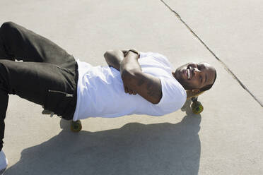 Afroamerikanischer Mann liegt auf einem Skateboard auf der Straße - BLEF07357