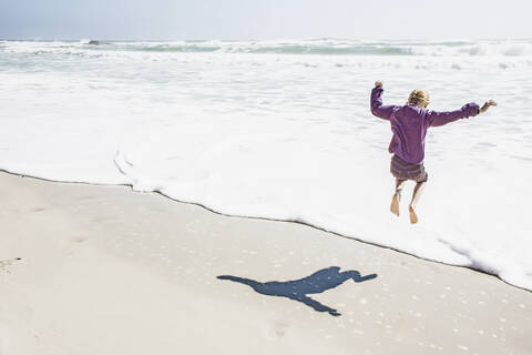 Mädchen spielt in den Wellen am sonnigen Strand, lizenzfreies Stockfoto