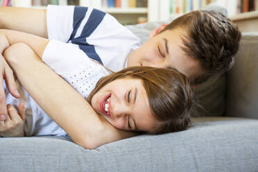 Portrait of laughing little girl lying together on couch with her older brother - LVF08115