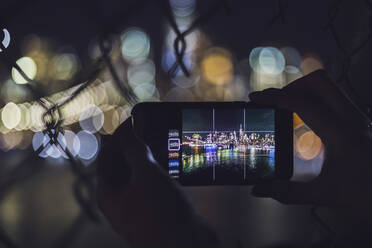 Nahaufnahme einer Frau, die mit ihrem Smartphone die nächtliche Skyline von Manhattan, New York City, USA, fotografiert - MMAF01053
