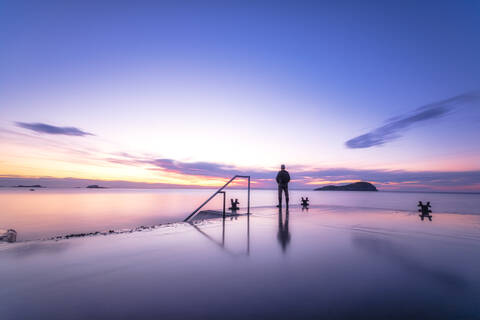 Mann steht allein am Hafenpier und beobachtet den Sonnenuntergang, North Berwick, East Lothian, Schottland, lizenzfreies Stockfoto