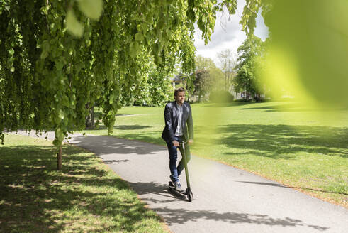 Businessman using E-Scooter in a park - JOSF03293