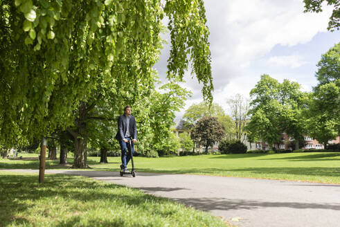 Businessman using E-Scooter in a park - JOSF03294