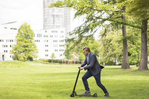 Geschäftsmann mit E-Scooter auf einer Wiese im Stadtpark, Essen, Deutschland - JOSF03303