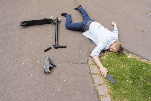 Accident victim lying on road besides E-Scooter and smartphone - JOSF03309