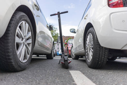 E-Scooter geparkt zwischen zwei Autos auf einem Parkplatz - JOSF03311