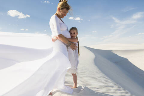 Schwangere kaukasische Mutter und Tochter, die sich in der Wüste umarmen, lizenzfreies Stockfoto