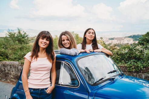Frau steht neben Freunden, die im Schiebedach eines Autos posieren, Florenz, Toskana, Italien - CUF51401