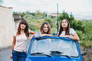 Frau steht neben Freunden, die im Schiebedach eines Autos posieren, Florenz, Toskana, Italien - CUF51403