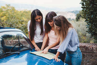 Freunde lesen die Straßenkarte auf der Motorhaube eines Autos in der Natur - CUF51404